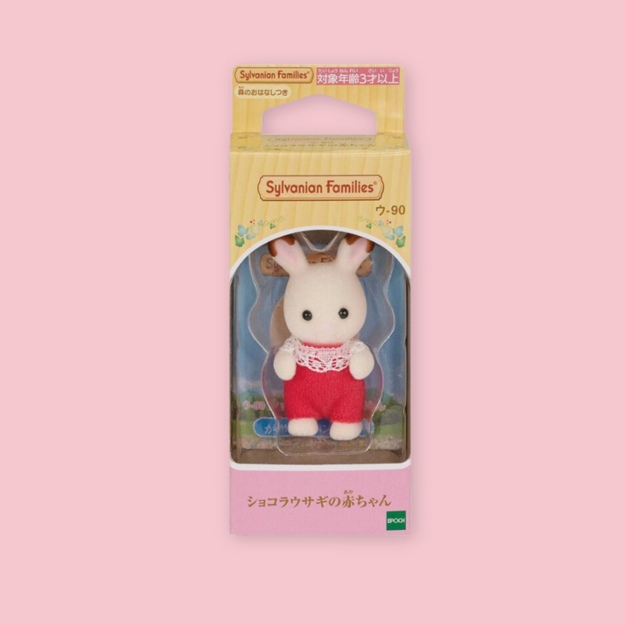 Baby Sylvanian Families chocolate rabbit figure in original Japanese box packaging, wearing a red outfit with white lace collar, photographed against a pastel pink background.