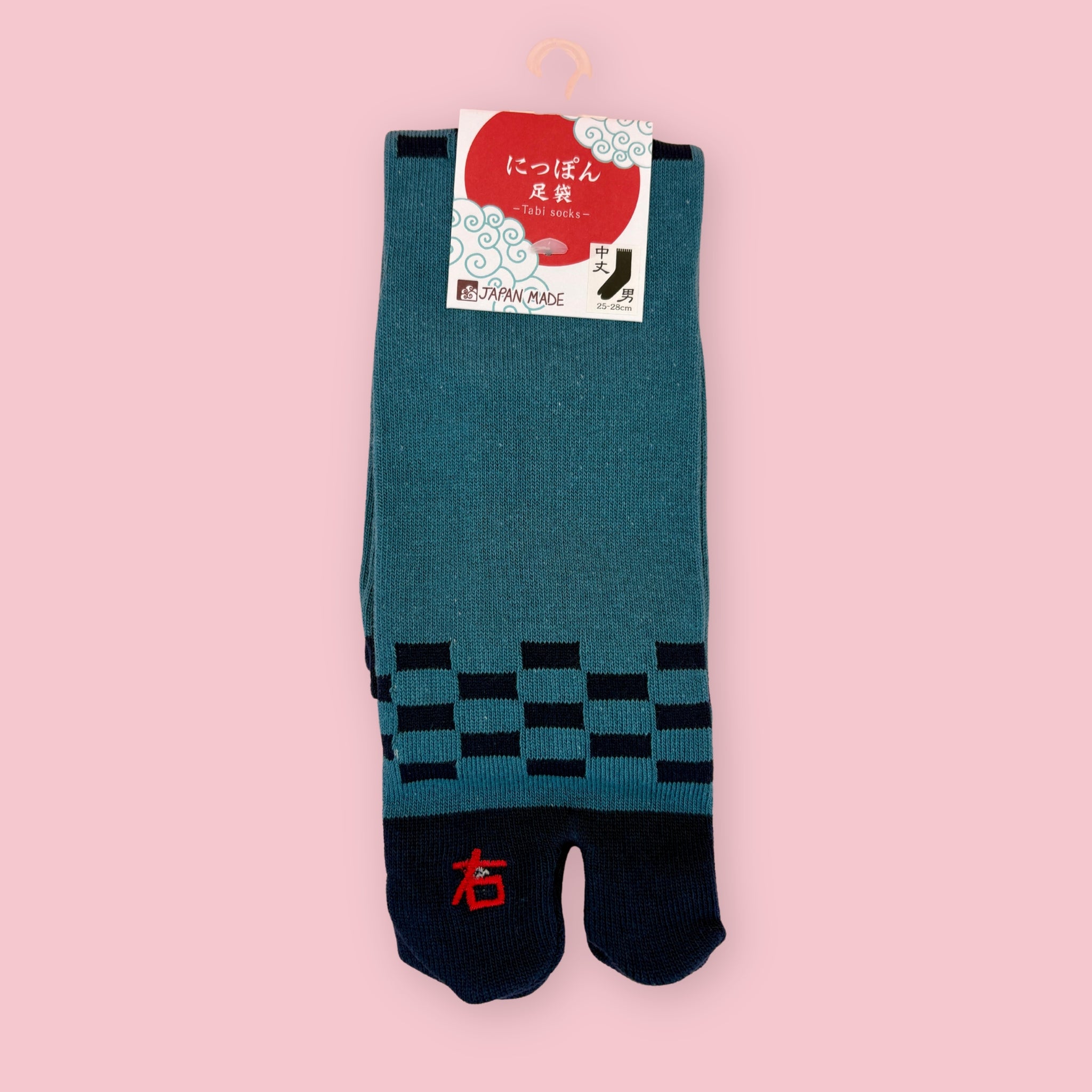 Teal and navy Japanese tabi socks with black checker pattern, shown in package against a pink background.
