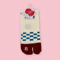 Cream and red Japanese tabi socks with blue checker pattern, shown in package against a pink background.