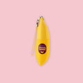TonyMoly Banana Lip Balm in a yellow banana-shaped tube with a hanging clip and strap, on a pink background.