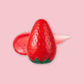 TonyMoly Strawberry Lip Balm in a strawberry-shaped container with green leaf detail, shown with a swipe of the balm beside it, on a pink background.