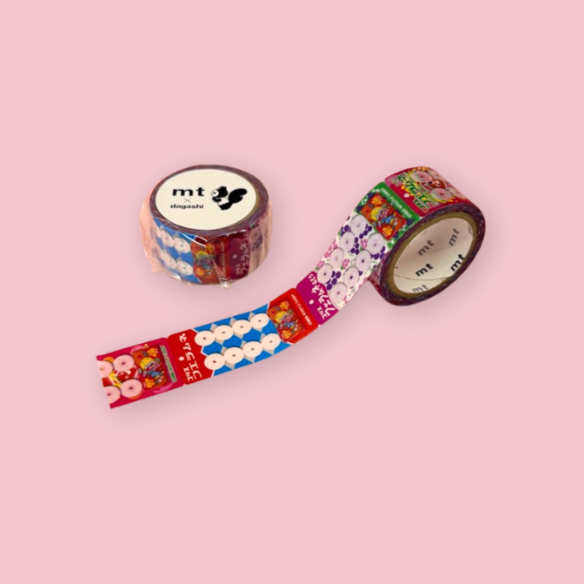 Two rolls of mt x dagashi washi tape with colorful Coris Fue Ramune candy packaging and whistle candy illustrations on a pastel pink background.
