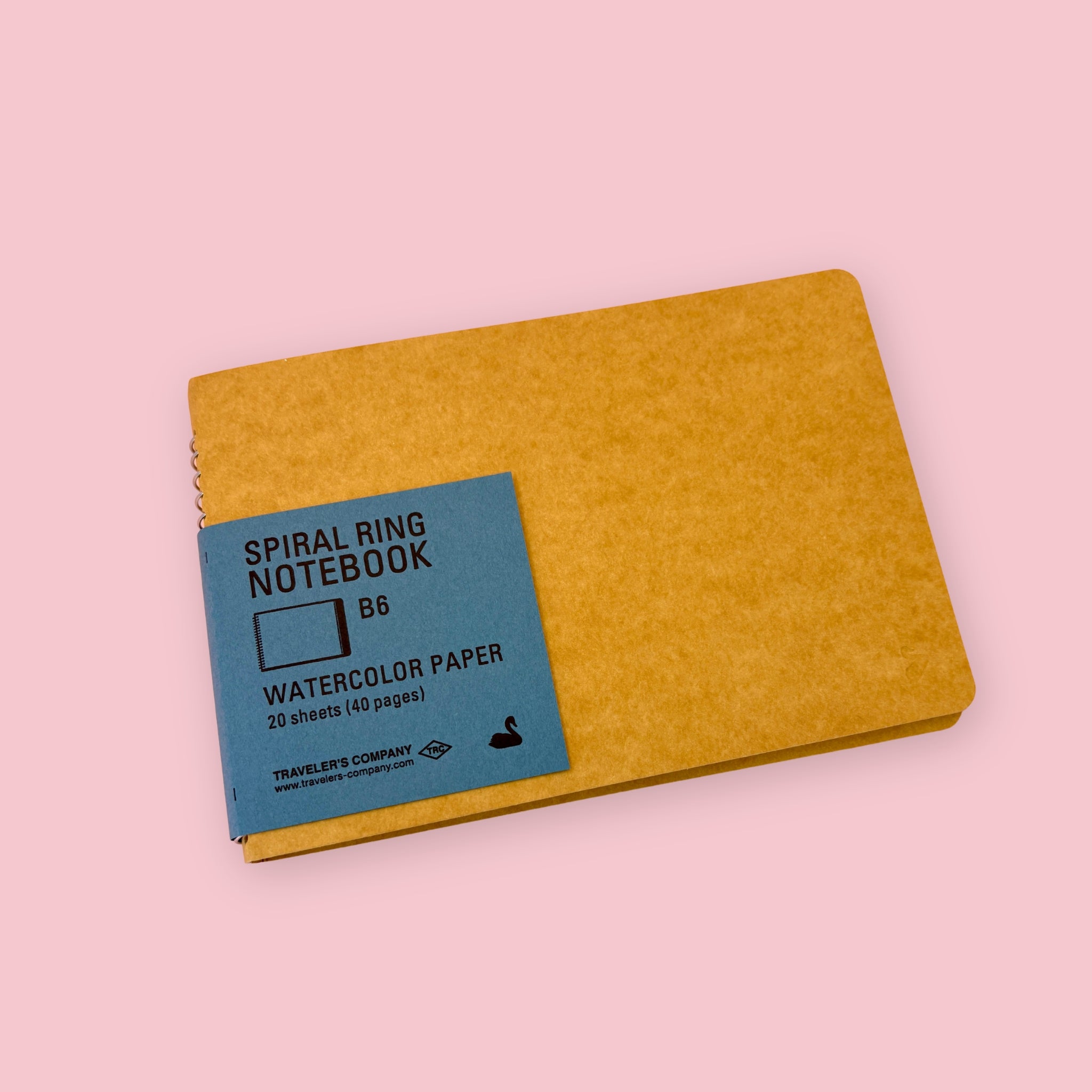 Kraft Traveler’s Company spiral ring watercolor notebook with blue label, shown against a pink background.
