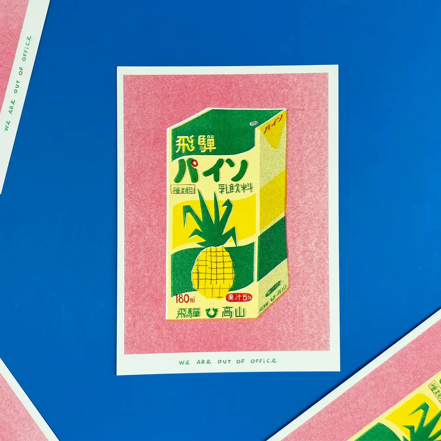We Are Out of Office risograph art print featuring a Japanese pineapple juice box illustration on a pink background, photographed against blue.