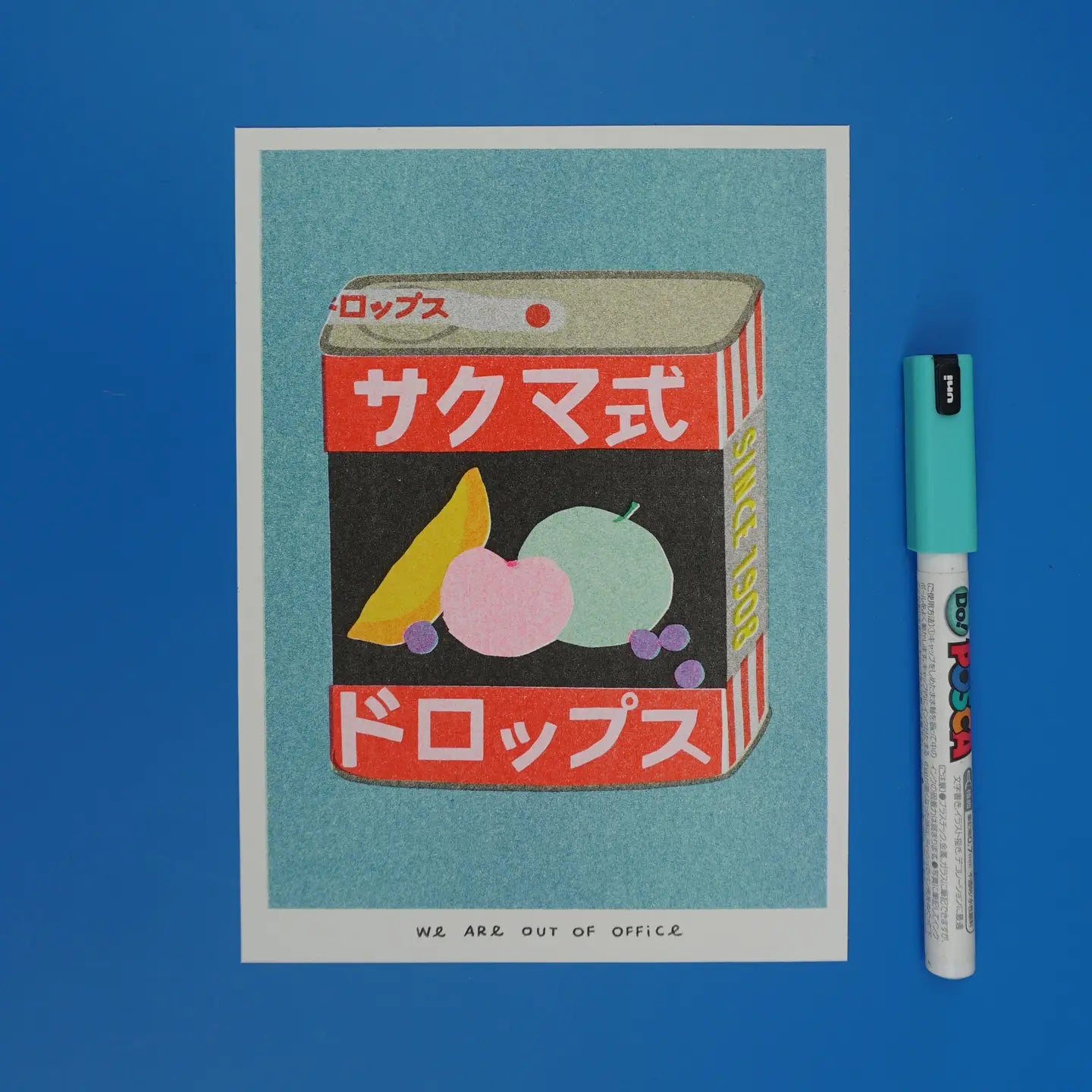 We Are Out of Office risograph art print featuring a vintage Sakuma Drops candy tin illustration with Japanese text, photographed on a blue background with a marker.
