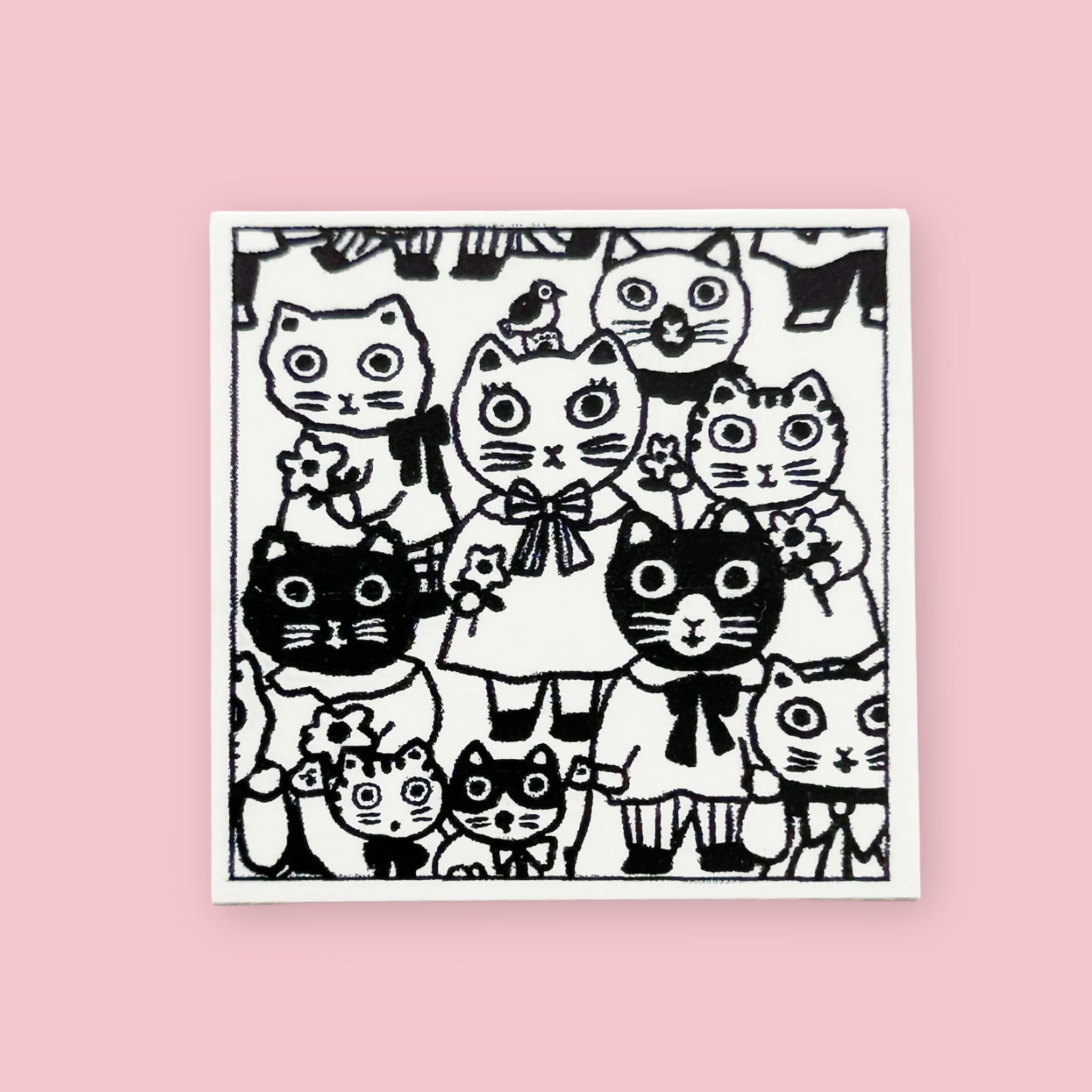 Yumi Kitagishi rubber stamp showing a crowd of wide-eyed cats in various sizes and outfits, including a central cat girl in a dress with a bow, printed in black ink on white paper, on a pink background.